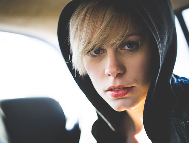An intense portrait of a young woman with a hooded sweatshirt, gazing directly at the camera with a mysterious expression.
