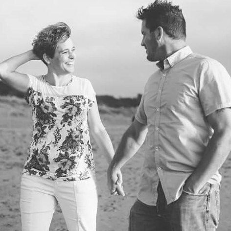 A smiling couple holds hands on the beach in black and white, enjoying a loving moment.
