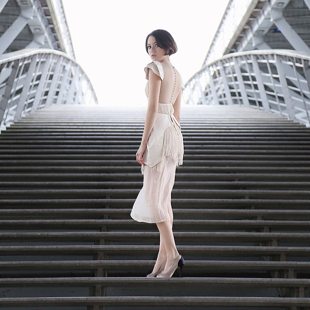 A woman in a dress poses on steps leading to a bridge.