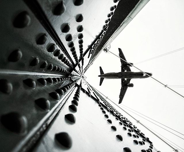 A low-angle shot of an airplane flying under a metallic bridge with a unique perspective.