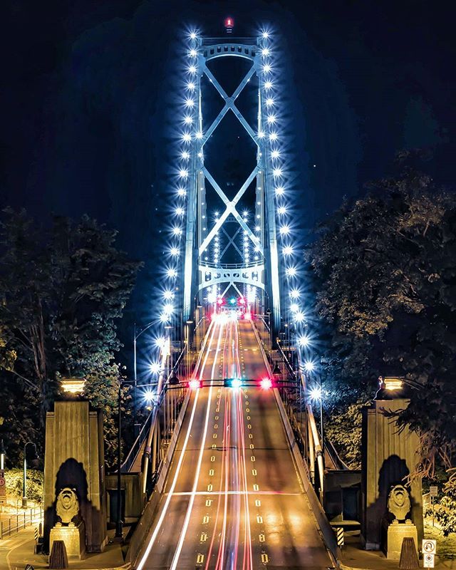 A long exposure shot of Lion's Gate Bridge at night, showcasing light trails and illuminated structure.