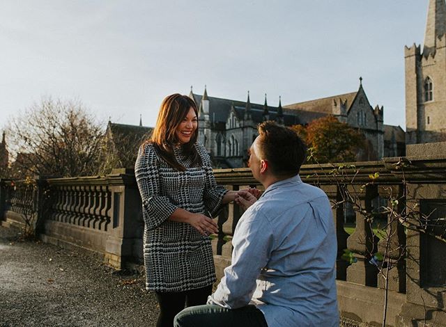 A man proposes to a woman with a building in the background on a sunny day.