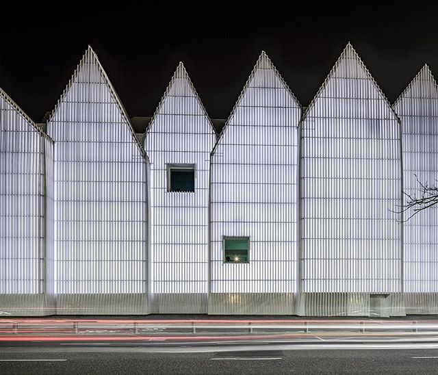 A modern building facade with unique triangular peaks stands illuminated at night, showcasing minimalist architecture.