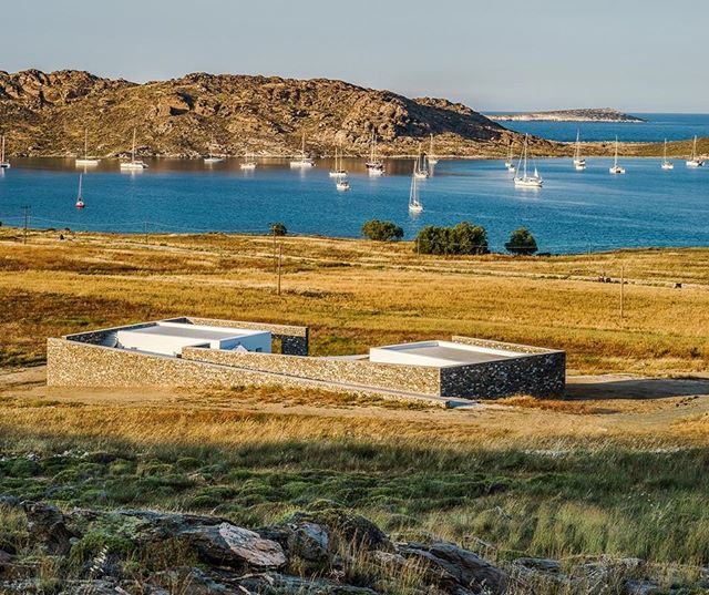Modern house blends into the coastal landscape with boats on a tranquil blue sea on a sunny day.