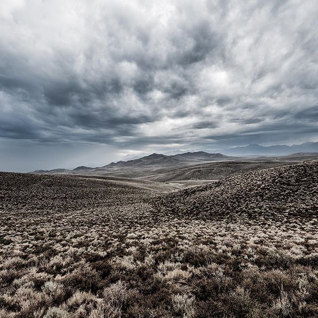 A dramatic landscape featuring rolling hills and mountains under a cloudy sky.