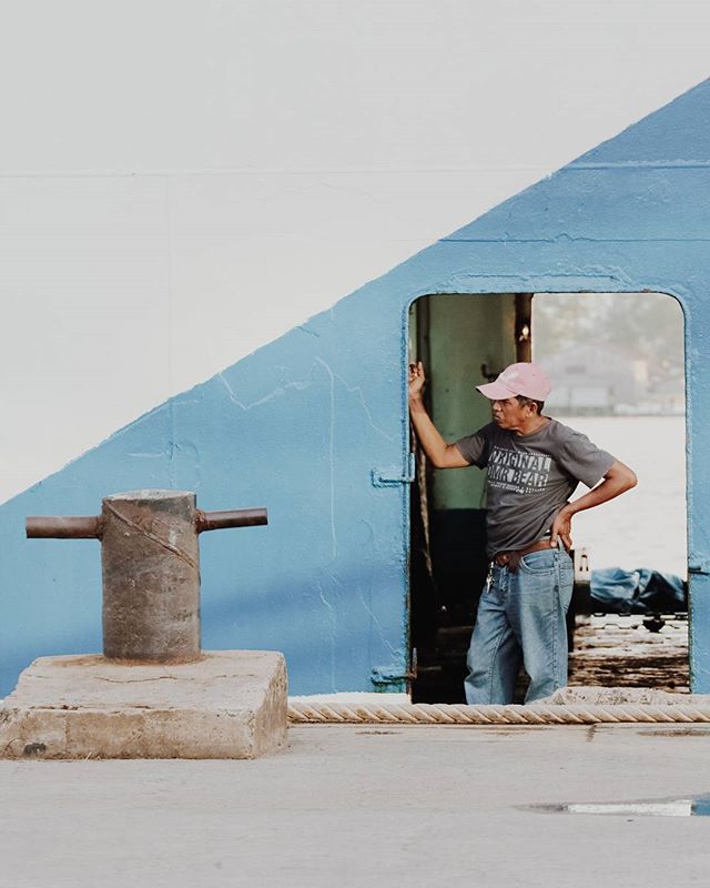 A man wearing a pink cap stands in a doorway near a bollard on a waterfront dock.