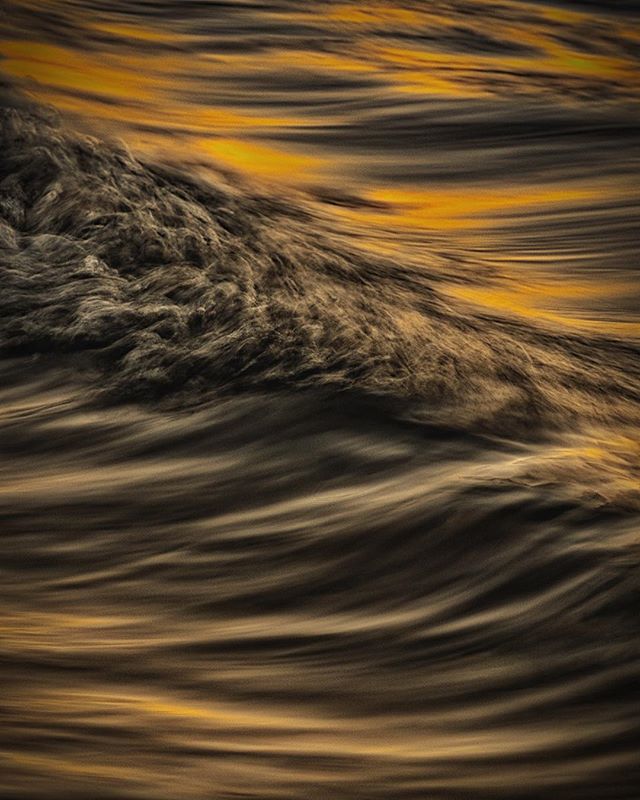 A close-up of ocean water in motion, creating an abstract pattern of browns, golds and blacks.