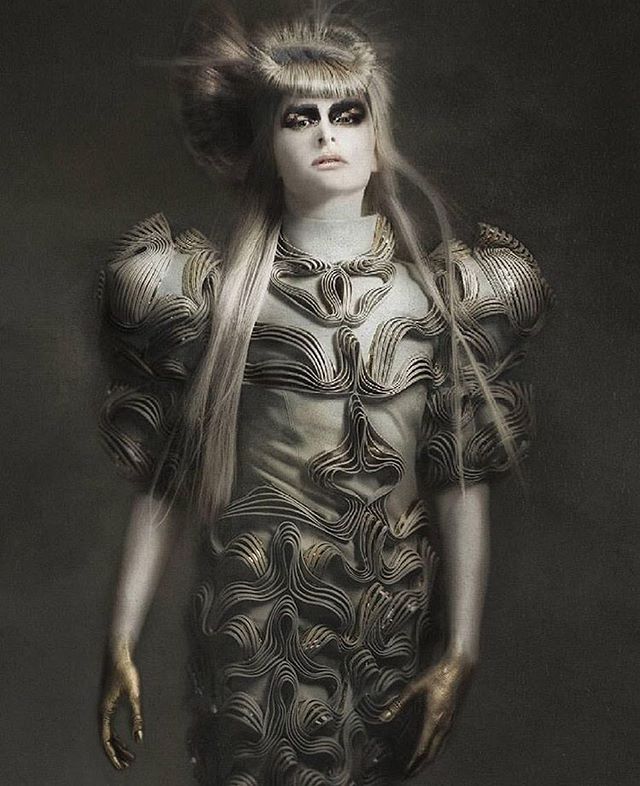 A woman showcases avant-garde fashion in a studio, with striking makeup and a unique gown for editorial or advertising use.