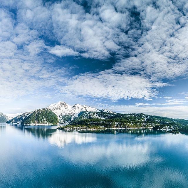 A scenic view of mountains reflecting on a tranquil lake under a partly cloudy sky.