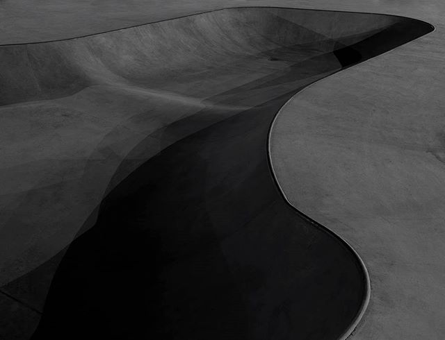 A high-angle view captures the curving lines and stark beauty of a modern, empty concrete skatepark bowl.