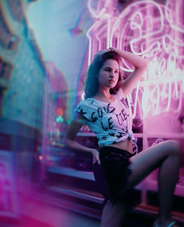 A woman poses by bright neon lights in the city, embodying urban energy and vibrant nightlife.