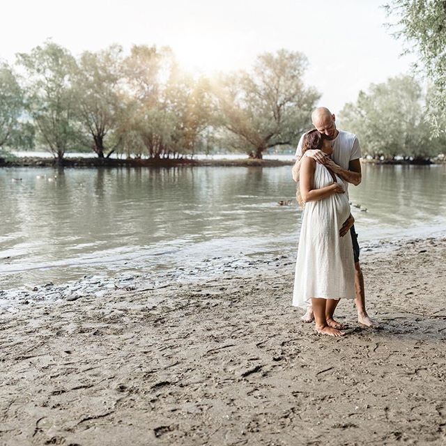 A pregnant woman and her partner share an intimate moment on a tranquil beach.