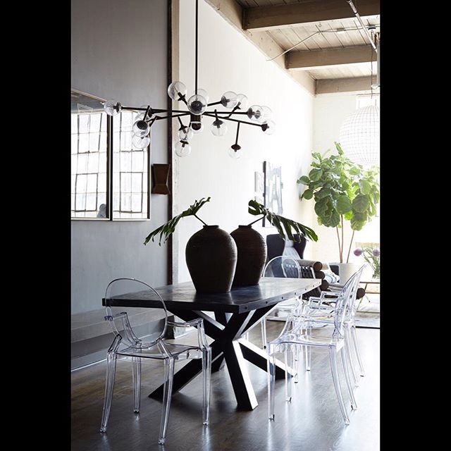 A modern dining room features a black table, clear chairs, and a unique chandelier.