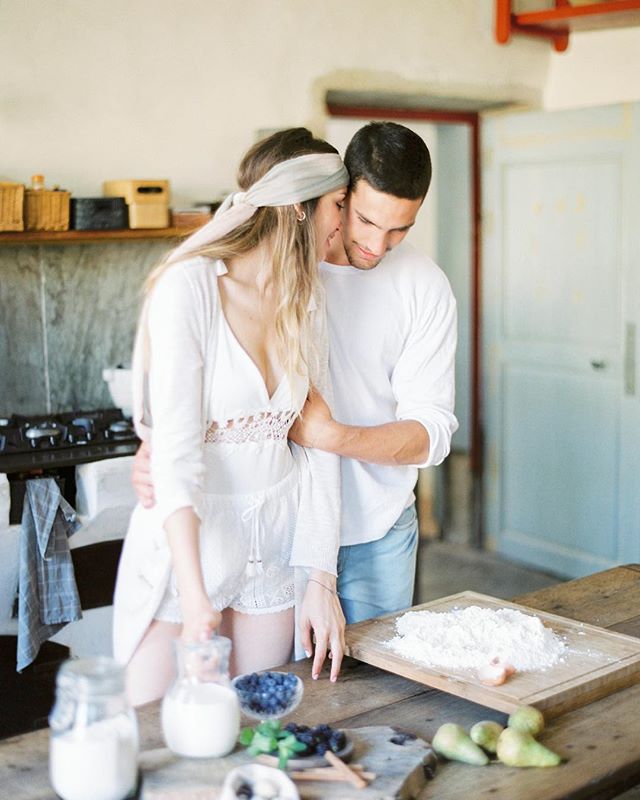 A loving couple embrace while preparing fresh ingredients together in a sun-lit kitchen.