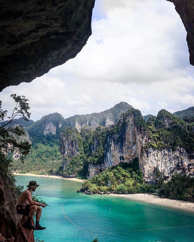Man sitting on a rock overlooking a tropical beach with turquoise water and mountains. 