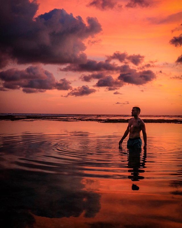 A man stands in calm ocean water at sunset, creating a serene and tranquil scene.