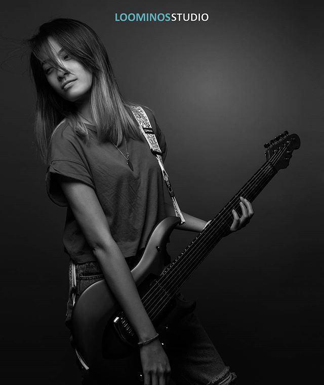 A stylish young woman plays a guitar in a modern studio setting in black and white.