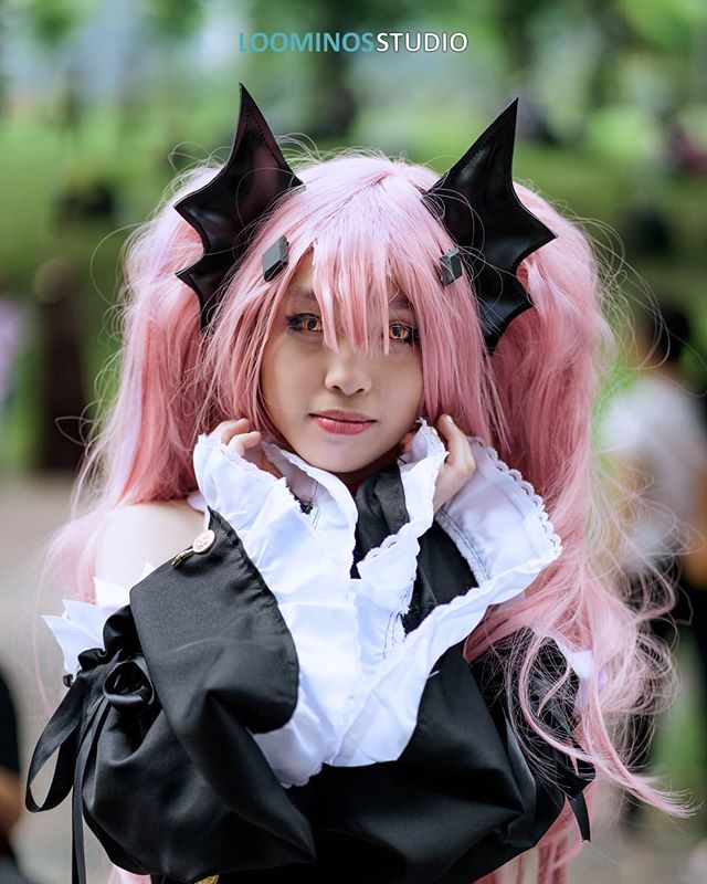 A woman with pink hair and a black and white costume poses for a cosplay portrait outdoors.