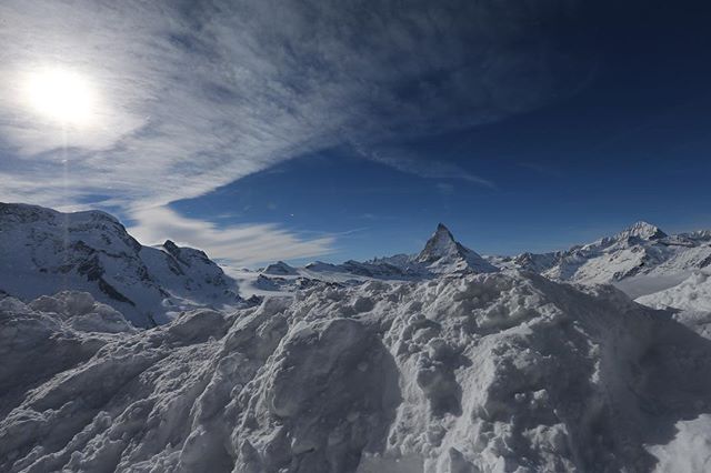 A scenic winter view of the Matterhorn mountain peak covered in snow against a bright blue sky.
