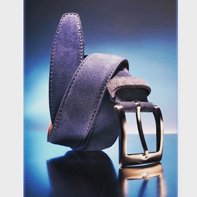 A stylish blue suede belt with a metal buckle is displayed against a cool-toned backdrop.