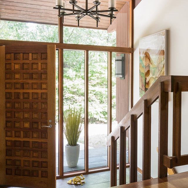 A well-lit modern entryway featuring a wooden door, plant, and staircase, blending interior design with natural light.