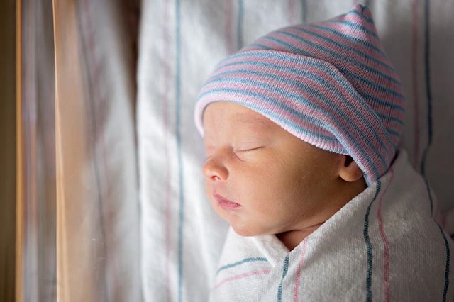 A newborn baby sleeps peacefully, wrapped in a blanket and wearing a striped hat.