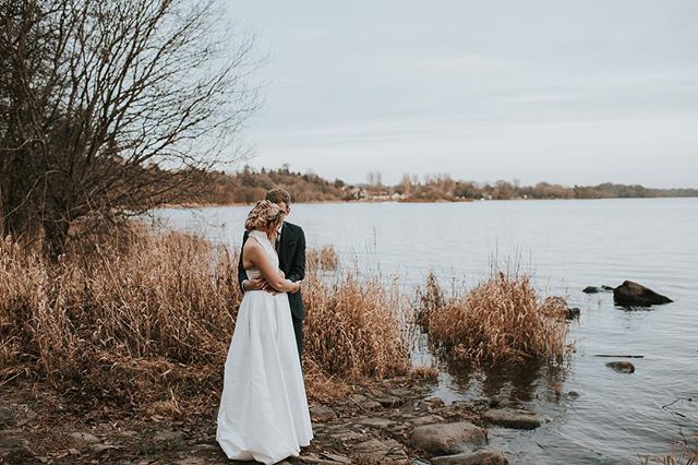 A bride and groom embrace by the lakeside in a romantic wedding scene.