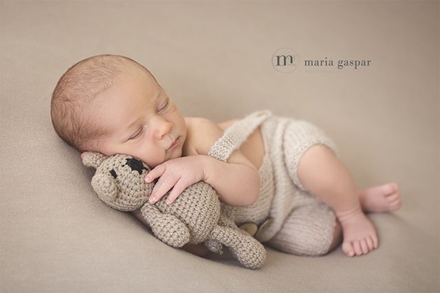 A newborn baby peacefully sleeps while cuddling a teddy bear.