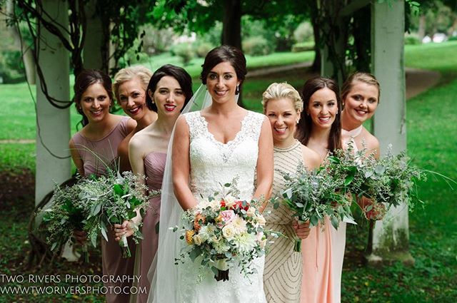 A bride and her bridesmaids pose with bouquets at an outdoor wedding celebration.