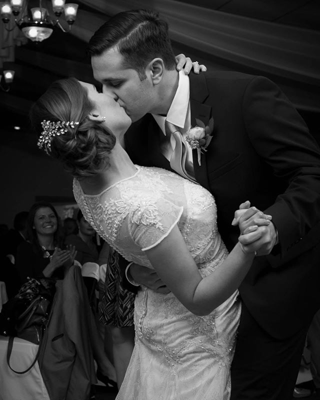 A bride and groom share a kiss during their first dance in a black and white wedding photograph.