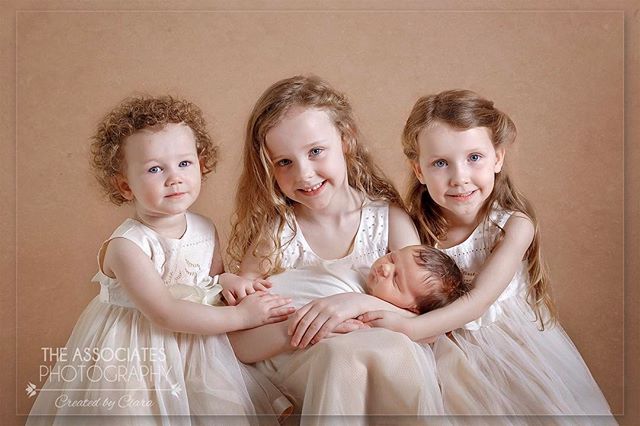 Three little girls gently cradle their newborn sibling in a heartwarming portrait, showcasing family love and a tender moment.