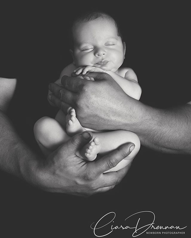 A newborn baby sleeps peacefully in parent's hands, in a tender, intimate studio portrait.