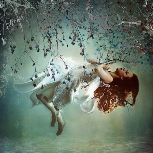 A woman in a white dress floats peacefully underwater, surrounded by ethereal light and tree branches in a dreamy scene.
