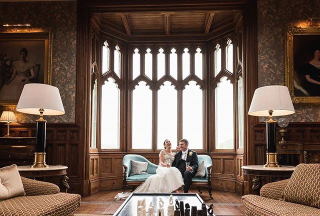 A happy couple laughs together on their wedding day in an elegant room with a large window.