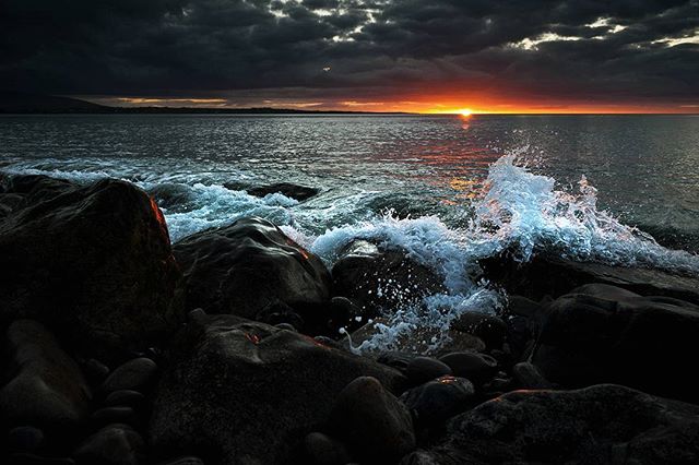 Waves crash on rocky shore under a dramatic sunset, creating a tranquil and scenic seascape.