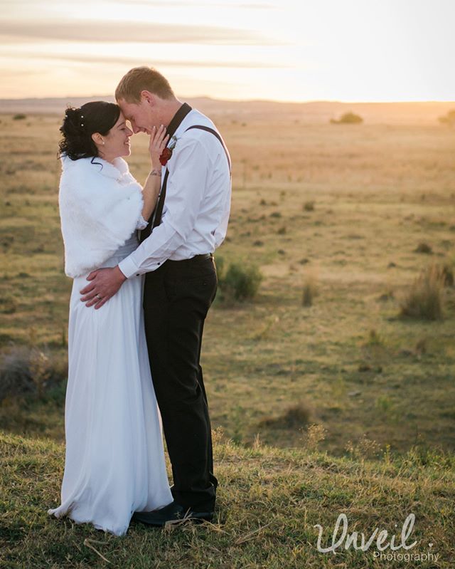 A bride and groom share an intimate moment in a field at sunset.