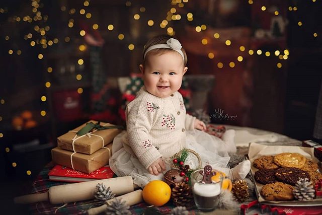 A cheerful baby girl celebrates the holidays with cookies and presents, radiating warmth and festive joy.