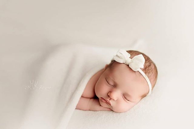 A serene newborn baby sleeps peacefully, wrapped in a soft blanket with a cute white bow headband.