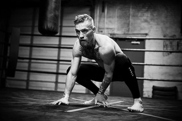 A focused athlete, Conor McGregor, trains in a monochrome gym setting, showcasing fitness and determination.