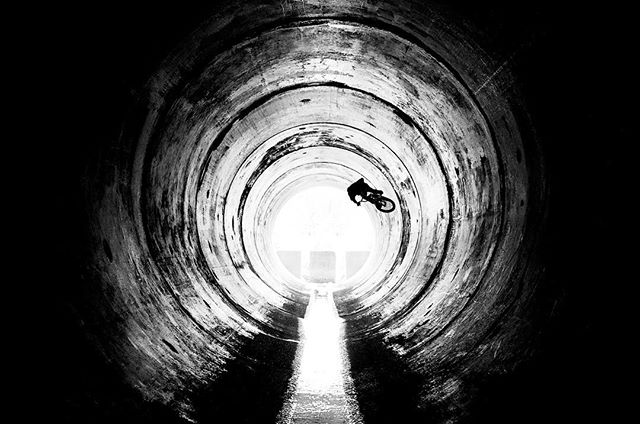 A lone cyclist rides through a dark tunnel, silhouetted against the light at the end.