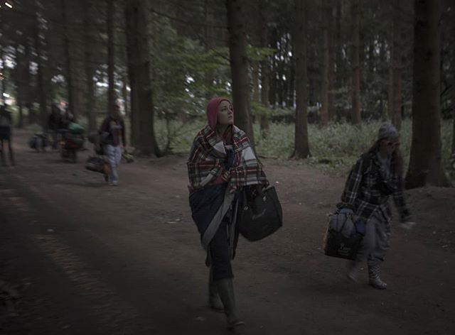 A group of people walk along a forest path wrapped in blankets in a natural outdoor setting.
