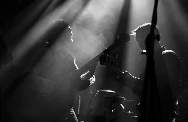 Two musicians are performing on a dimly lit stage in black and white.