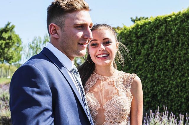 A happy couple poses outdoors in formal attire, sharing a cheerful moment in a garden setting.