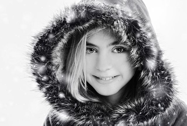 A serene, black-and-white portrait of a girl in a fur-trimmed hood in a winter setting.