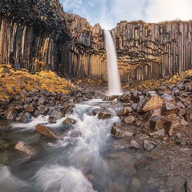 A scenic view of a waterfall cascading down basalt columns into a rocky stream in Iceland.