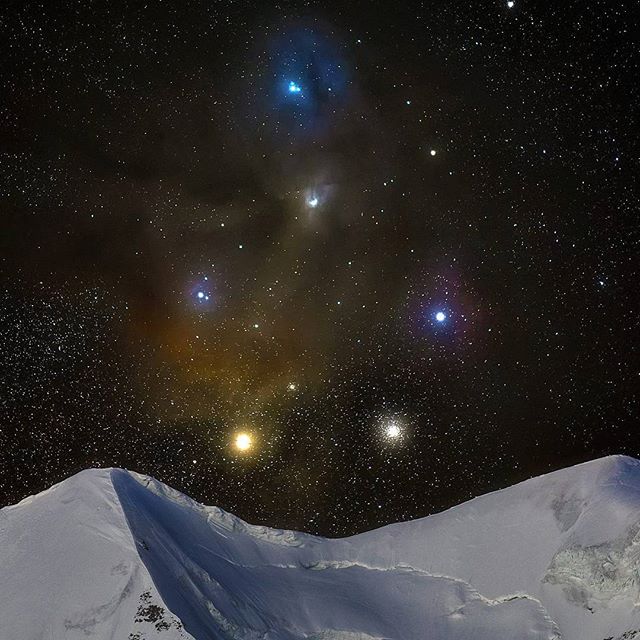 A starry night sky illuminates the snowy mountain peaks, creating a serene and majestic landscape.