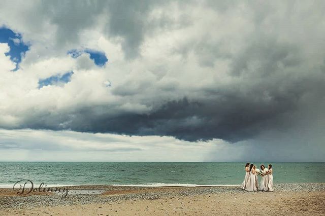 Bridesmaids stand on a beach under a cloudy sky in a dreamy, soft shot perfect for wedding planning and destination advertising.