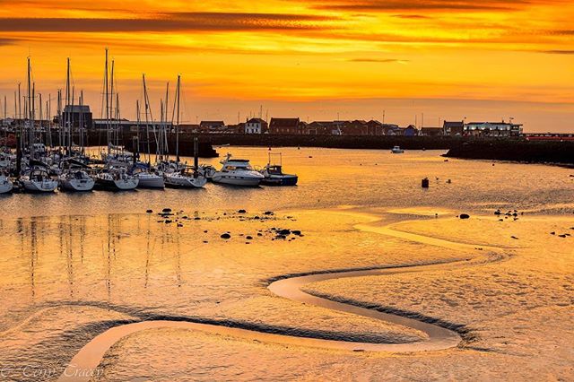 Golden sunset over a marina with sailboats and a winding tidal channel. Calm seascape perfect for travel and coastal themes.
