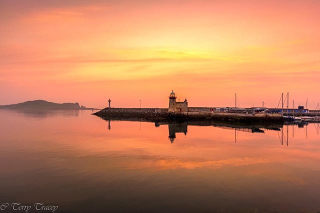 Picturesque harbor scene featuring a lighthouse silhouetted against a colorful sunrise, perfect for travel and tourism campaigns.