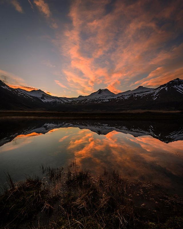 A tranquil lake reflects a colorful sunset sky and snow-capped mountains creating a serene landscape scene.